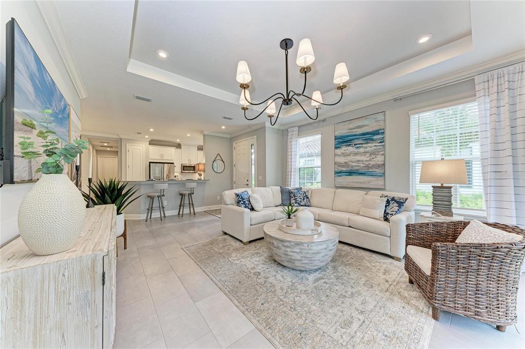A bright living room features a white sectional sofa, a round coffee table, and a chandelier — 15712 SACILE LANE, BRADENTON, FL