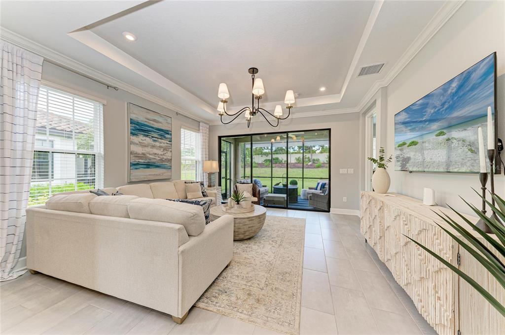 A bright living room features a sectional sofa, a chandelier, and sliding doors to a patio — 15712 SACILE LANE, BRADENTON, FL