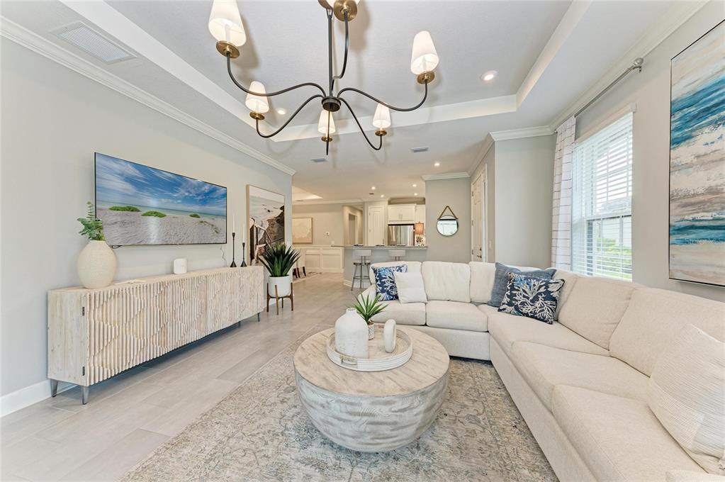 A bright living room features a sectional sofa, a round coffee table, and a chandelier — 15712 SACILE LANE, BRADENTON, FL