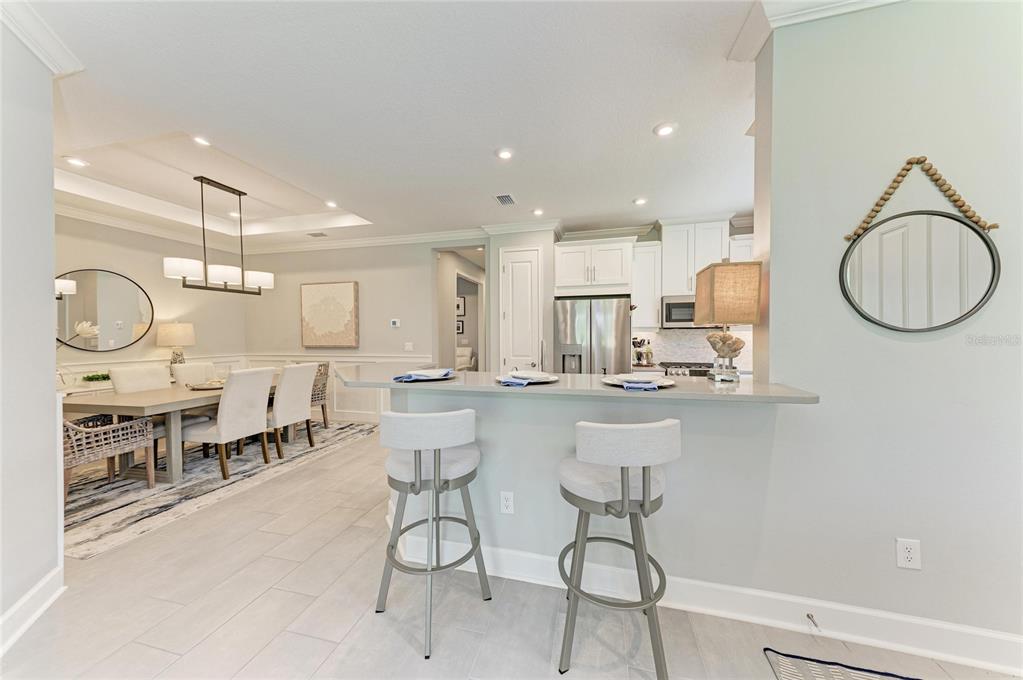 A kitchen with a breakfast bar and stools overlooks a dining area with a chandelier — 15712 SACILE LANE, BRADENTON, FL