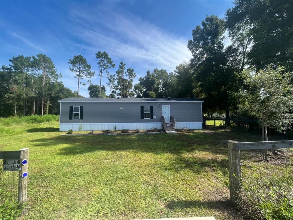 A single-story manufactured home with gray siding stands on a grassy lot with trees — 11347 NW 12TH LANE, OCALA, FL