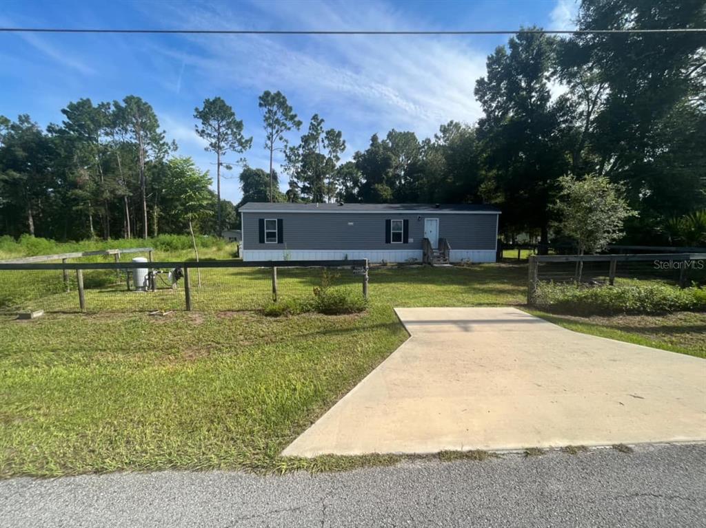 A gray manufactured home sits on a grassy lot behind a wooden fence and driveway — 11347 NW 12TH LANE, OCALA, FL