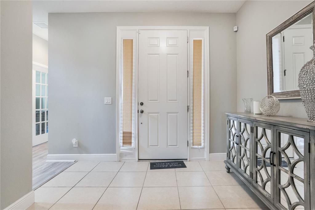 A bright entryway features a white front door with sidelights, tile flooring, and a console table — 1321 WILDCAT LANE, MINNEOLA, FL
