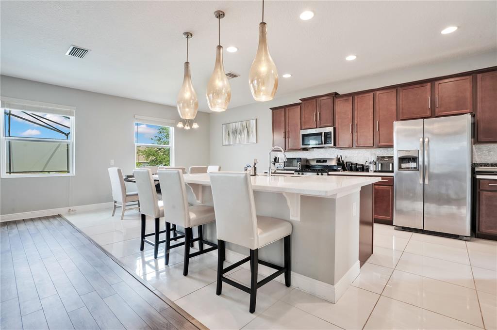 A kitchen with a white island, bar stools, stainless steel appliances, and dark wood cabinets — 1321 WILDCAT LANE, MINNEOLA, FL
