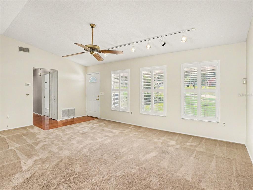 A carpeted living room features a ceiling fan, track lighting, and three windows with shutters — 7207 IMMOKALEE COURT, ORLANDO, FL