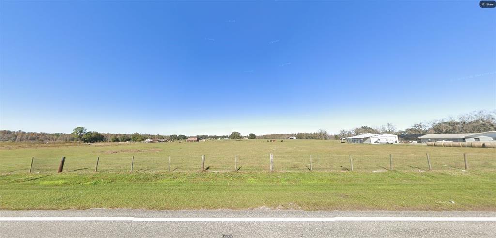 A wide, grassy field is enclosed by a wire fence under a clear blue sky — OLD POLK CITY RD, POLK CITY, FL