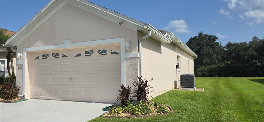A beige house exterior features a two-car garage, a side air conditioning unit, and landscaping — 3630 KARIBA COURT, KISSIMMEE, FL