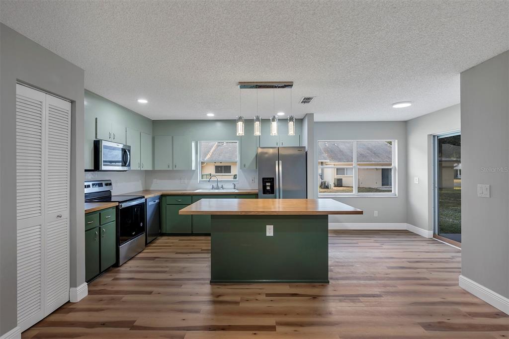 A kitchen features green cabinets, a wooden island, stainless steel appliances, and wood-look flooring — 9755 SW 94TH TERRACE UNIT C, OCALA, FL