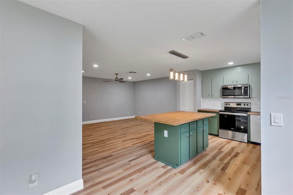 An open-concept kitchen and living area features green cabinets, a wood-topped island, and light wood flooring — 9755 SW 94TH TERRACE UNIT C, OCALA, FL