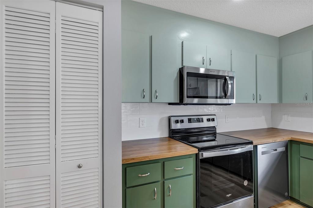 A kitchen features green lower cabinets, light blue upper cabinets, wood countertops, and stainless appliances — 9755 SW 94TH TERRACE UNIT C, OCALA, FL