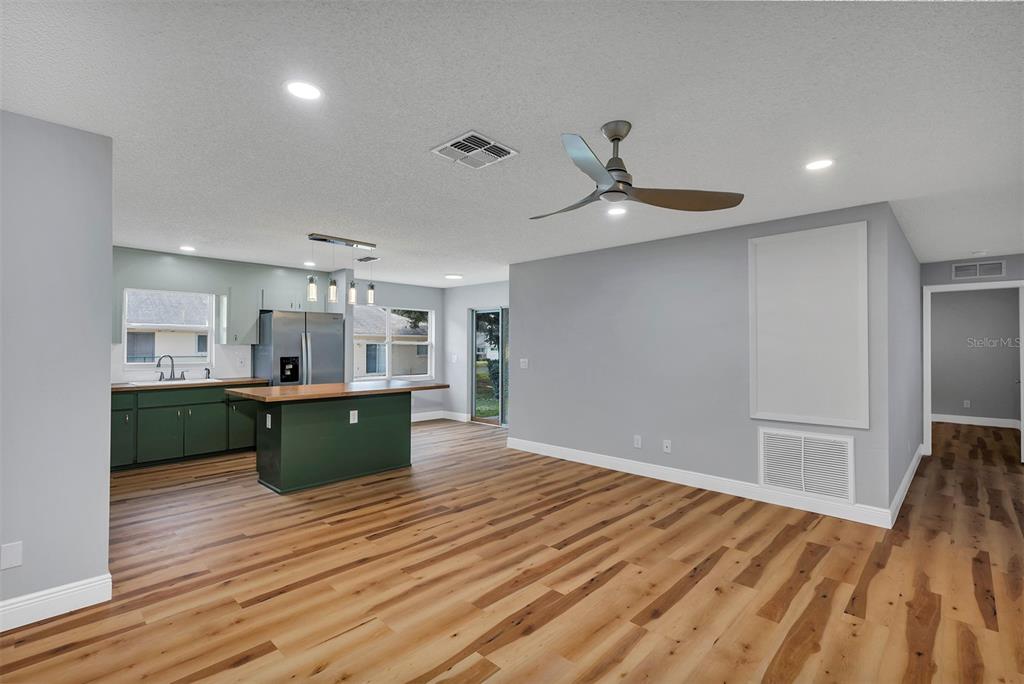 An open-concept kitchen and living area features green cabinets, a wood island, and wood flooring — 9755 SW 94TH TERRACE UNIT C, OCALA, FL