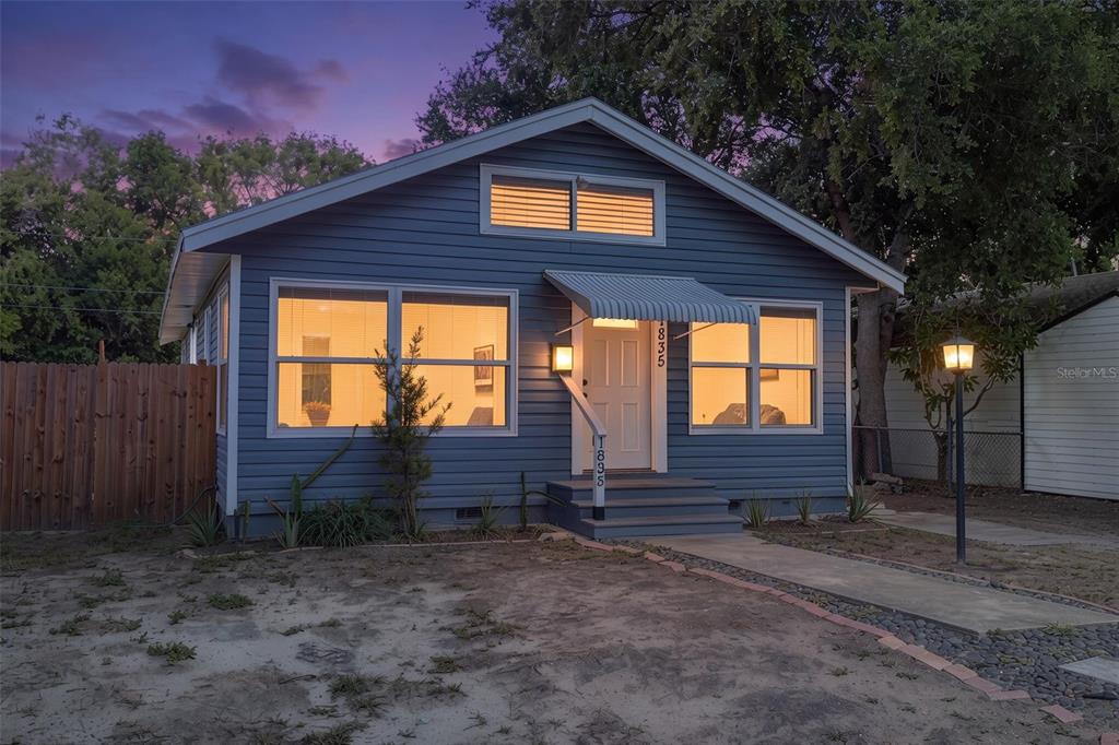 A blue, single-story house with a gabled roof, front porch awning, and illuminated windows at dusk — 1835 47TH STREET S, ST PETERSBURG, FL
