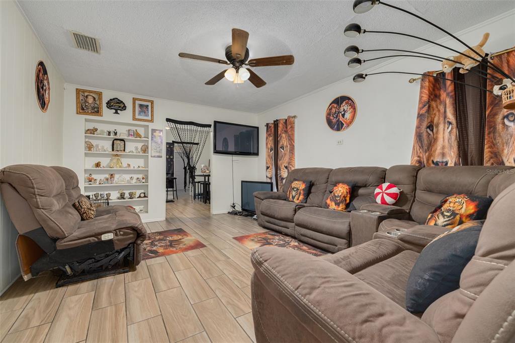 A living room features tile flooring, brown reclining sofas, a ceiling fan, and built-in shelving — 1835 47TH STREET S, ST PETERSBURG, FL