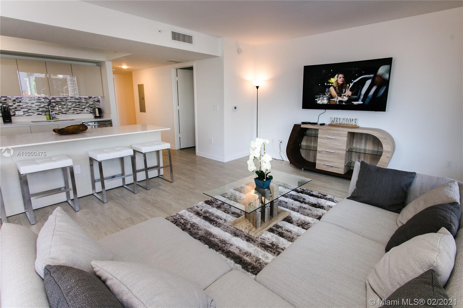 A modern living room features a sectional sofa, glass coffee table, and an open kitchen — 2600 E Hallandale Beach Blvd, Hallandale Beach FL 33009, HALLANDALE BEACH, FL