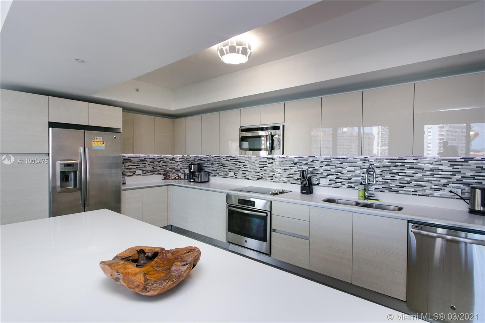 A modern kitchen features light wood cabinetry, stainless steel appliances, and a white island countertop — 2600 E Hallandale Beach Blvd, Hallandale Beach FL 33009, HALLANDALE BEACH, FL