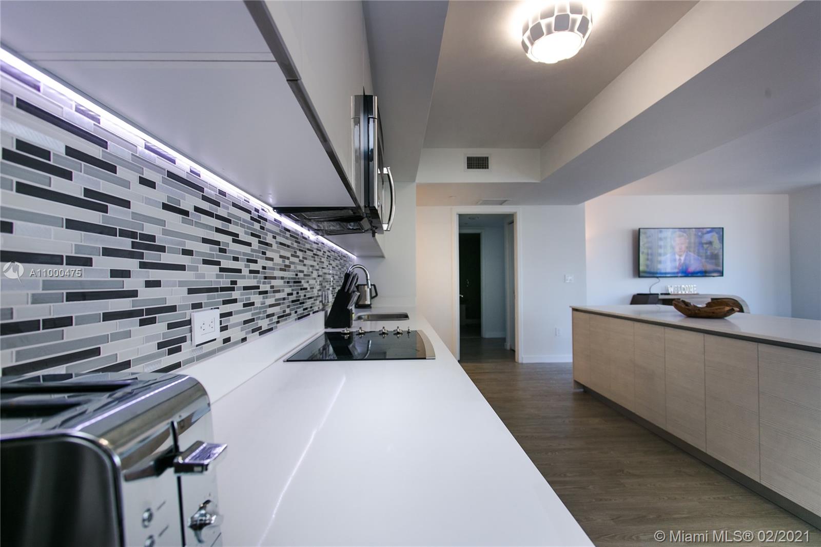 A modern kitchen features white countertops, a mosaic tile backsplash, and a wooden island — 2600 E Hallandale Beach Blvd, Hallandale Beach FL 33009, HALLANDALE BEACH, FL