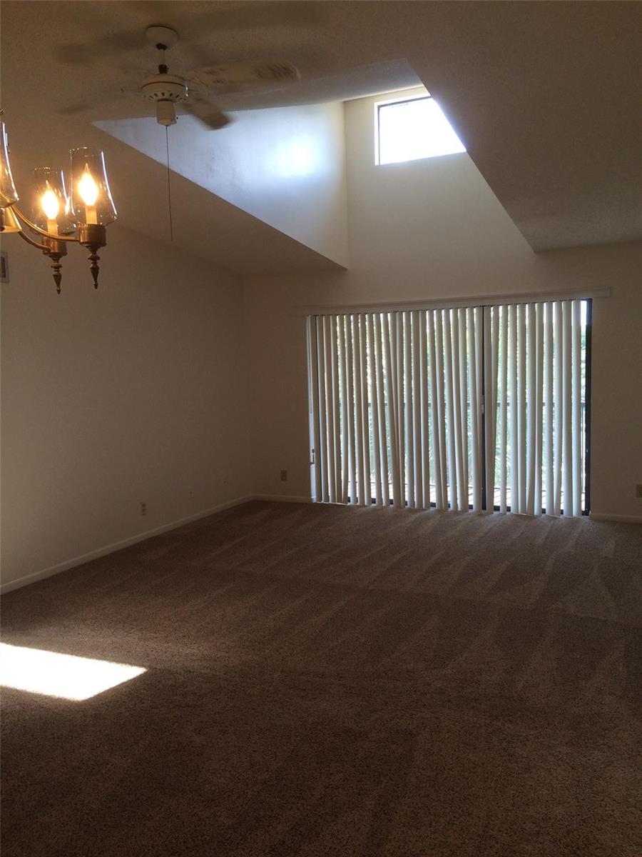A living room with beige carpet, a vaulted ceiling, a skylight, and vertical window blinds — 209 Foxtail Drive # 3, FL 33415, FL