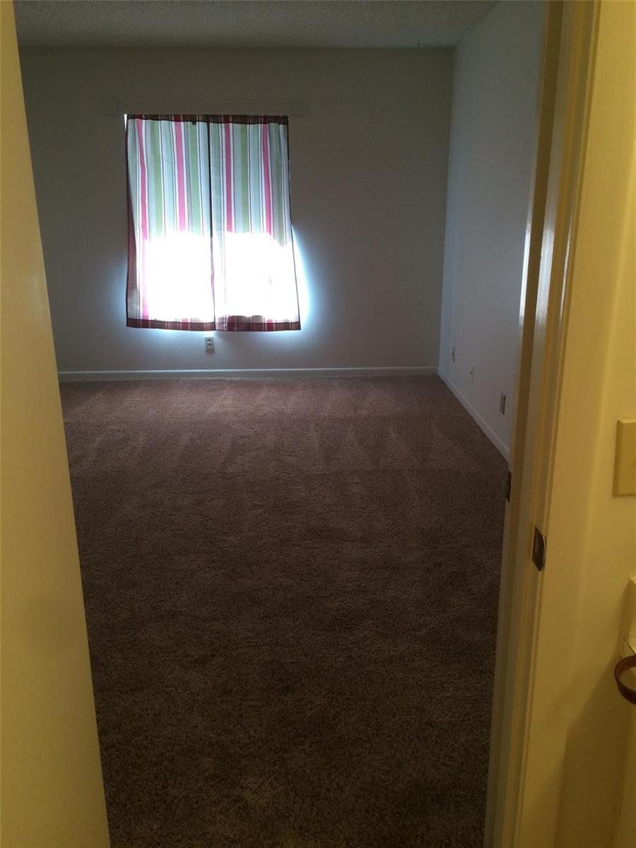 A view through a doorway into an empty bedroom with beige carpet and striped curtains — 209 Foxtail Drive # 3, FL 33415, FL