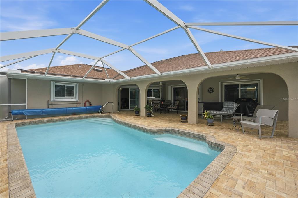 A swimming pool with a screened enclosure sits on a paved patio beside a house — 25378 RUPERT ROAD, PUNTA GORDA, FL