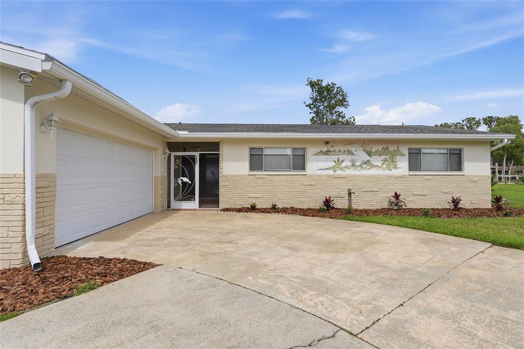 A single-story house with a white garage door, tan brick facade, and a decorative wall mural — 1401 SE PARADISE AVENUE, CRYSTAL RIVER, FL