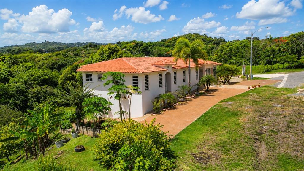 A two-story house with a red tile roof sits on a grassy, sloped hillside — Car 416 km 2.3 PIEDRAS BLANCAS, AGUADA, PR