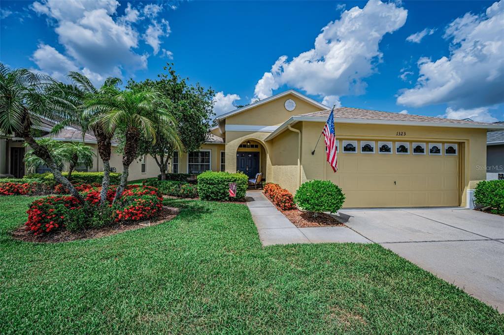 A single-story yellow house with a two-car garage, palm trees, and a landscaped front yard — 1323 WINDING WILLOW DRIVE, TRINITY, FL