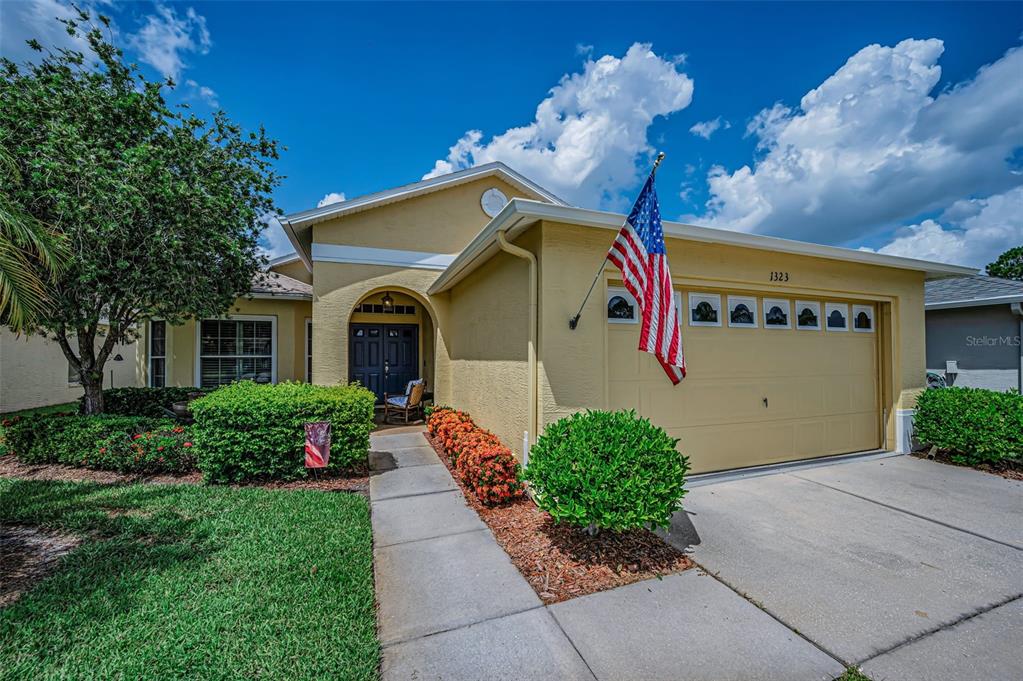 A yellow single-story house with a two-car garage and an American flag in front — 1323 WINDING WILLOW DRIVE, TRINITY, FL
