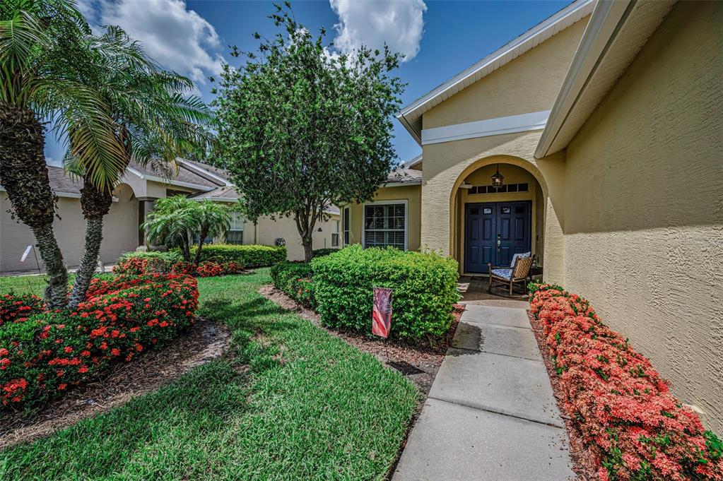 A walkway leads to the front entrance of a house with yellow stucco walls — 1323 WINDING WILLOW DRIVE, TRINITY, FL