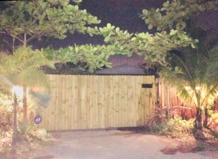 A wooden privacy fence stands in front of a house at night with surrounding trees — 250 NE 13th Street, Delray Beach FL 33444, DELRAY BEACH, FL