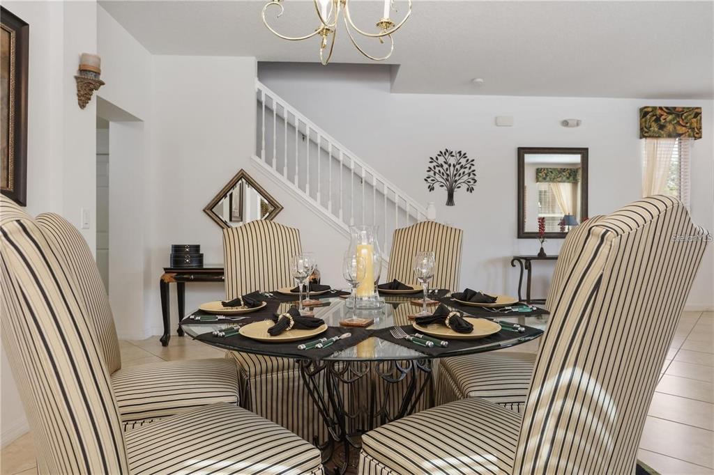 A dining room features a glass-topped table with striped chairs and a staircase nearby — 4515 STELLA STREET, KISSIMMEE, FL