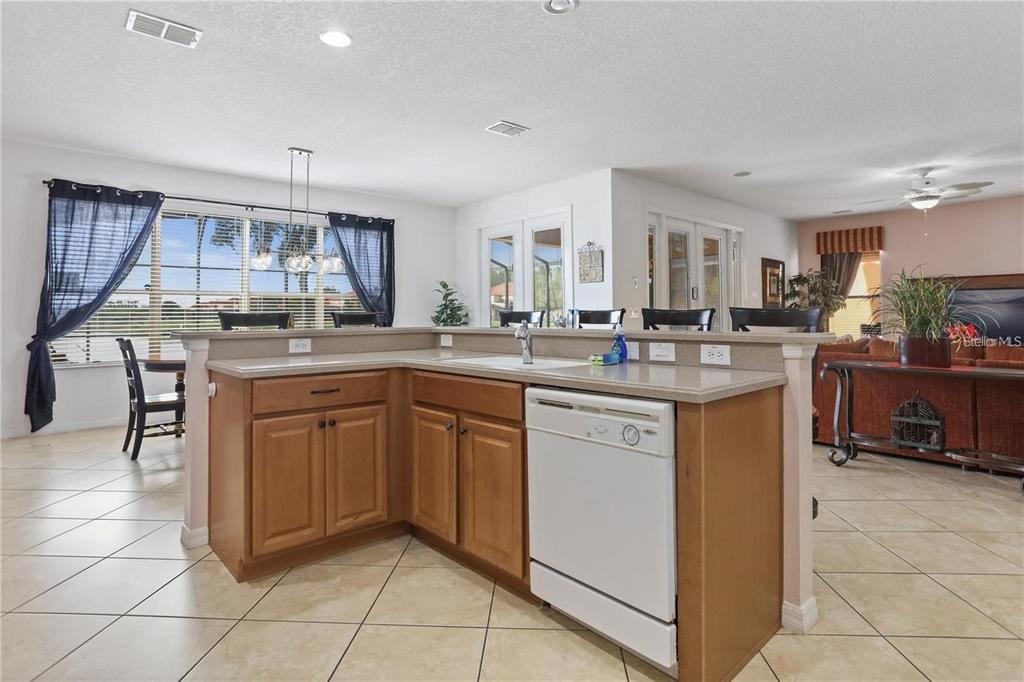 A kitchen island with a white dishwasher and wood cabinets sits before a dining area — 4515 STELLA STREET, KISSIMMEE, FL