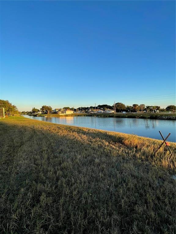 A grassy bank overlooks a canal with houses visible in the distance under a clear sky — 470 & 472 BOUNDARY BOULEVARD, ROTONDA WEST, FL