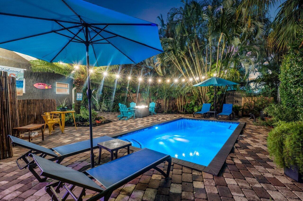 A backyard patio features a swimming pool, lounge chairs, umbrellas, and string lights at night — 1911 Parker Avenue, West Palm Beach FL 33401, WEST PALM BEACH, FL