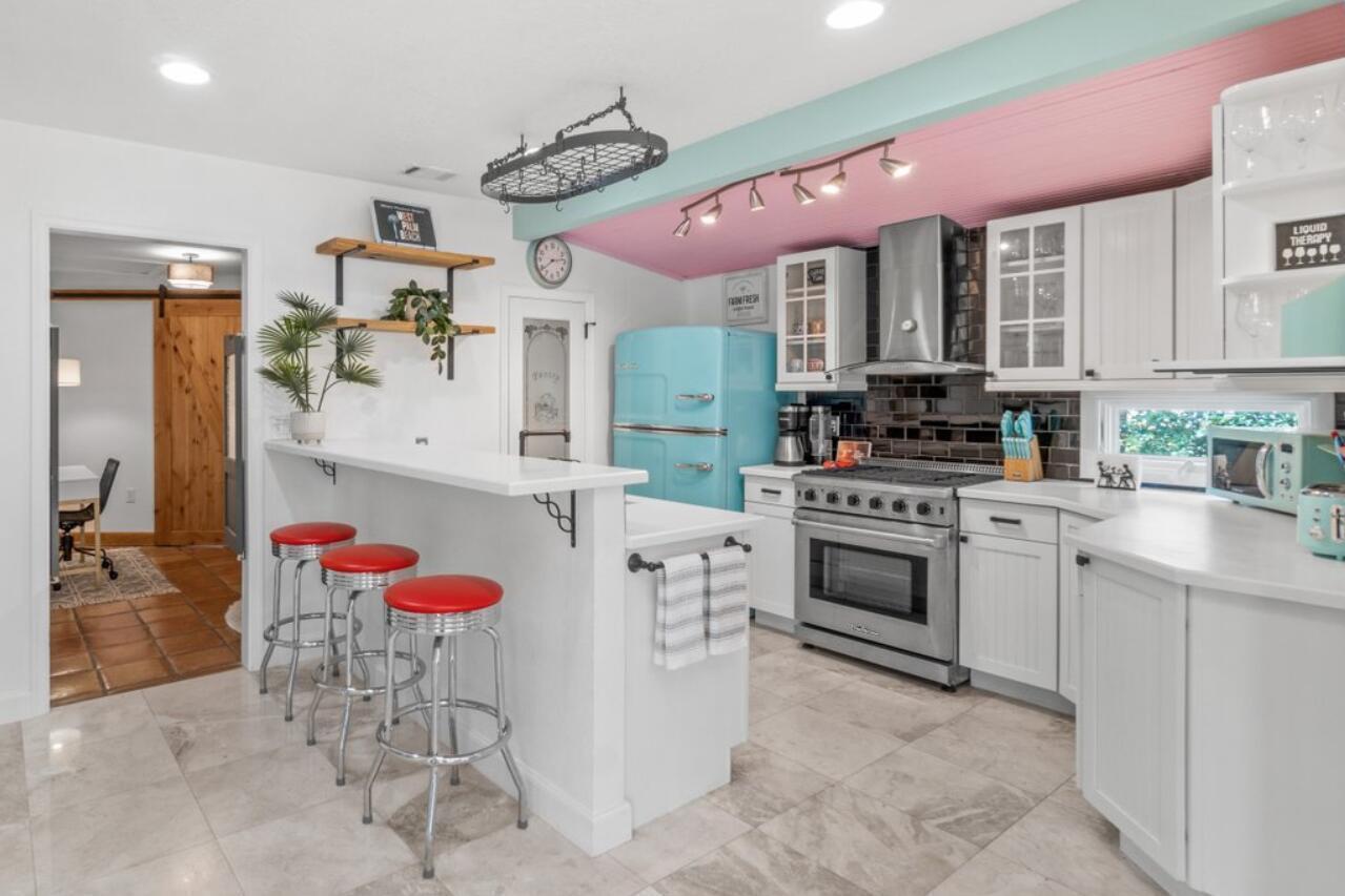 A kitchen features white cabinets, a retro blue refrigerator, red bar stools, and pink ceiling — 1911 Parker Avenue, West Palm Beach FL 33401, WEST PALM BEACH, FL