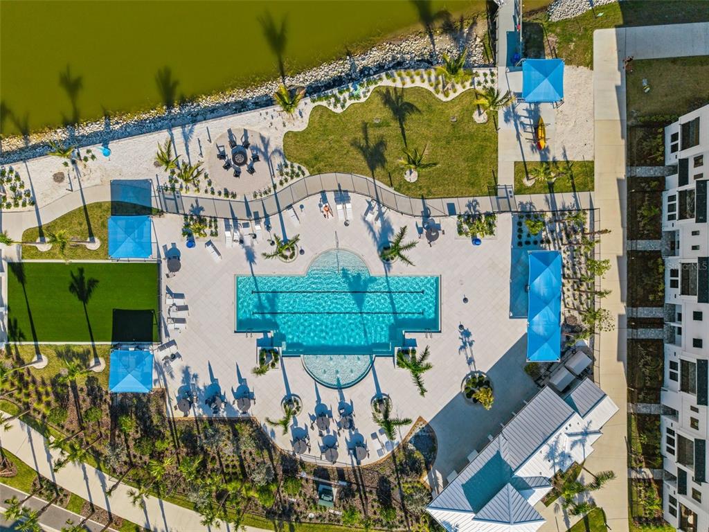 An aerial view shows a swimming pool with lounge chairs, cabanas, and a nearby lake — 7244 SUTTON LANE, SARASOTA, FL