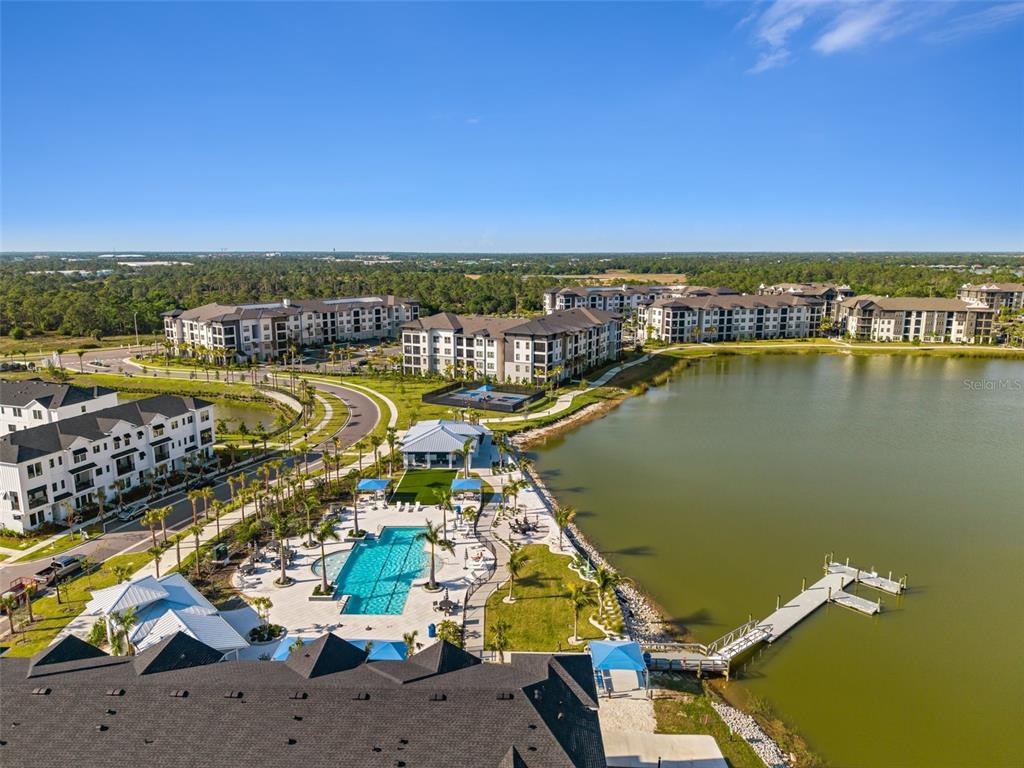 An aerial view shows a multi-story apartment complex with a pool, clubhouse, and lake — 7244 SUTTON LANE, SARASOTA, FL