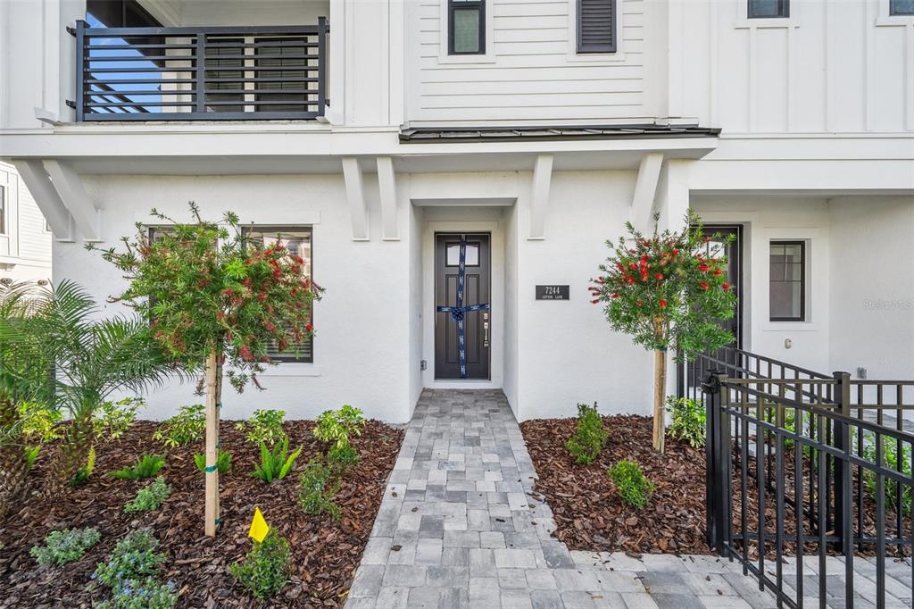 A paved walkway leads to the front entrance of a white two-story townhouse — 7244 SUTTON LANE, SARASOTA, FL