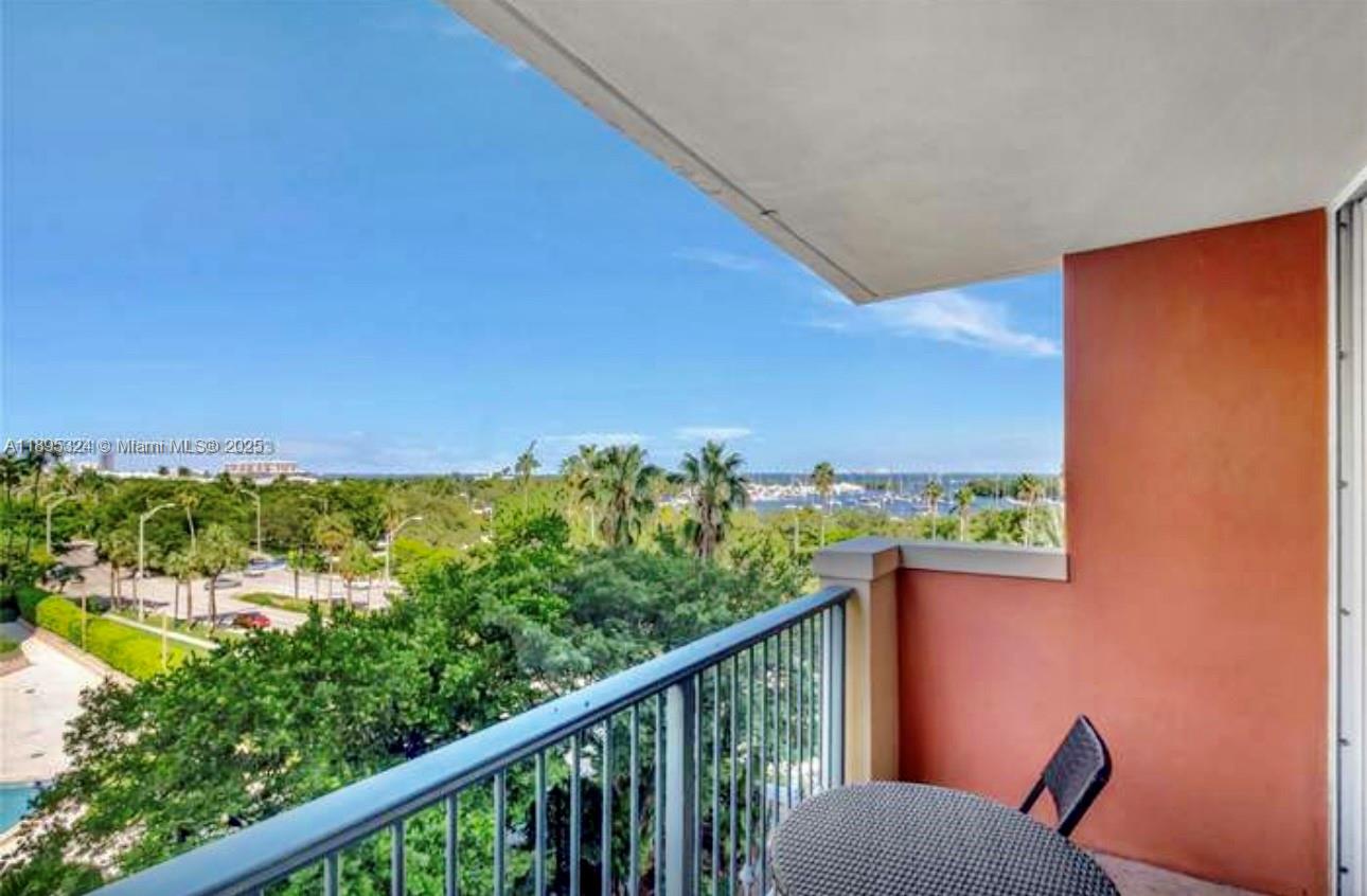 A balcony with a metal railing overlooks a park, trees, and a distant body of water — 2951 S Bayshore Dr # 603, Miami FL 33133, MIAMI, FL