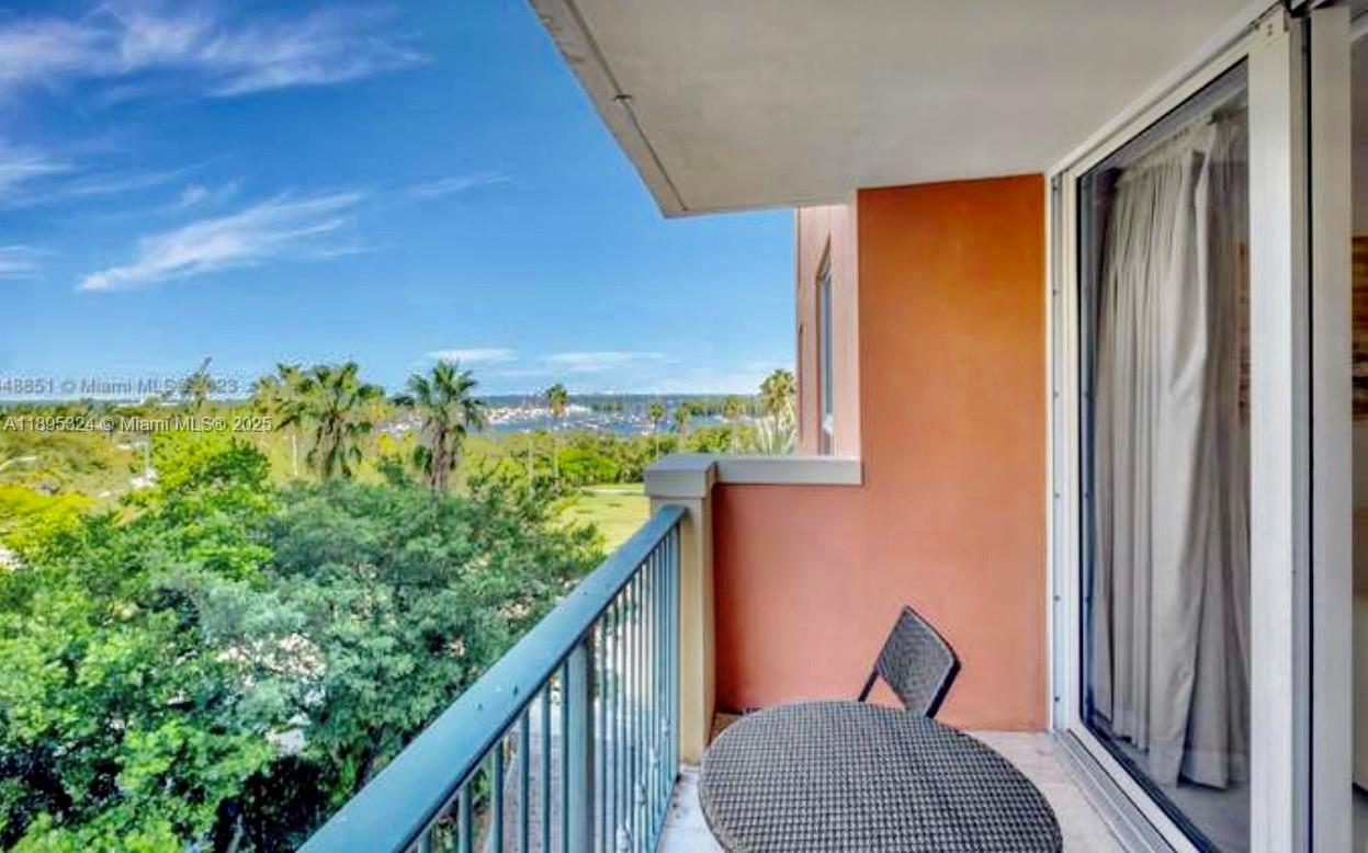 A balcony with a metal railing overlooks a green landscape and a distant body of water — 2951 S Bayshore Dr # 603, Miami FL 33133, MIAMI, FL