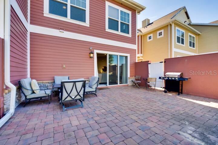 A paved patio features outdoor furniture and a grill against a red exterior wall — 7583 SUNNY DREAMS LANE, KISSIMMEE, FL