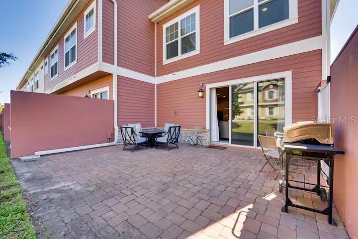 A paved patio features outdoor furniture and a grill next to a multi-story building — 7583 SUNNY DREAMS LANE, KISSIMMEE, FL