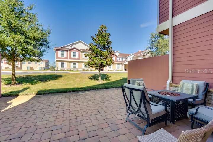 A paved patio features outdoor furniture with a view of nearby apartment buildings and trees — 7583 SUNNY DREAMS LANE, KISSIMMEE, FL