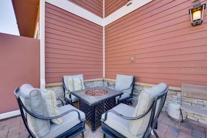 A patio features four chairs arranged around a square fire pit against a red-sided wall — 7583 SUNNY DREAMS LANE, KISSIMMEE, FL