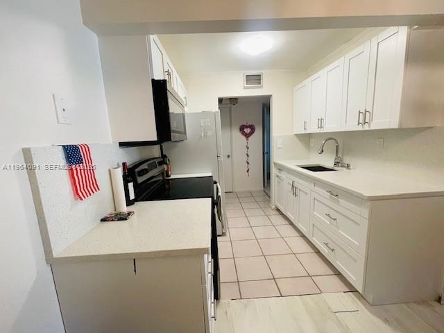 A kitchen features white cabinets, light countertops, stainless steel appliances, and tiled flooring — 5180 E Sabal Palm Blvd # 235, Tamarac FL 33319, TAMARAC, FL