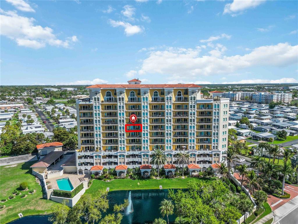 An aerial view of a multi-story yellow apartment building with a pool and pond — 501 HABEN BOULEVARD UNIT 704, PALMETTO, FL