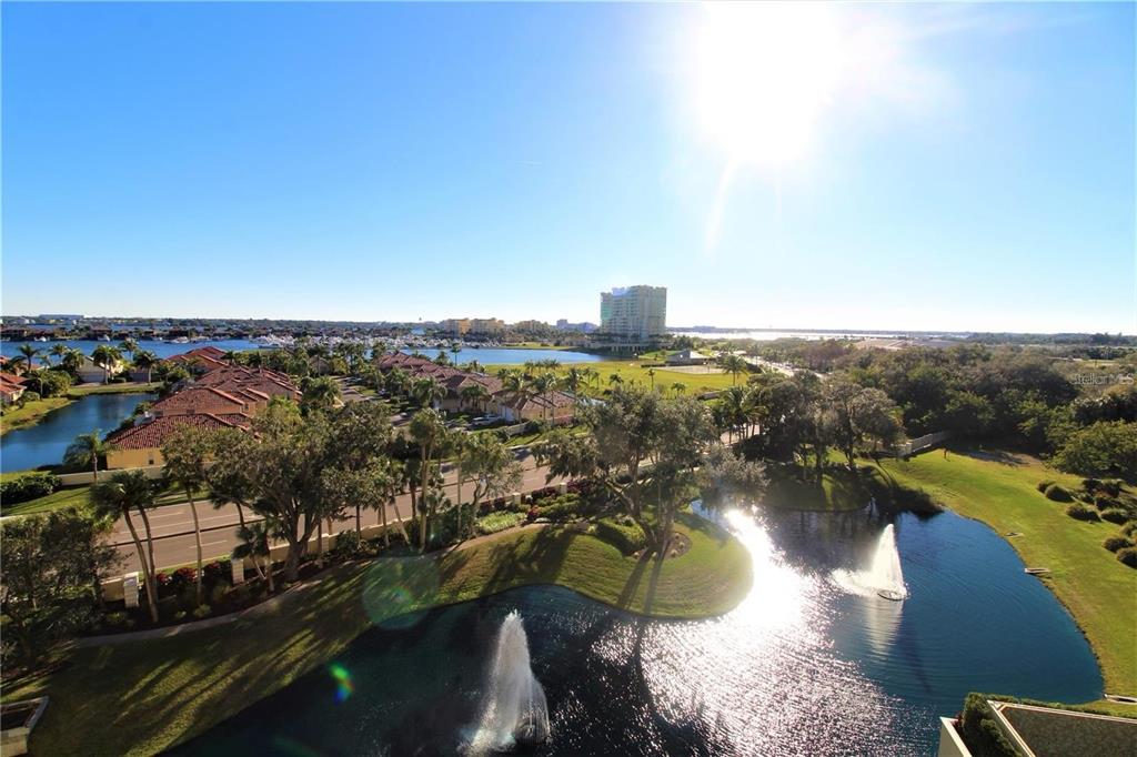 An elevated view of a pond with fountains, surrounding landscaping, and distant residential buildings — 501 HABEN BOULEVARD UNIT 704, PALMETTO, FL