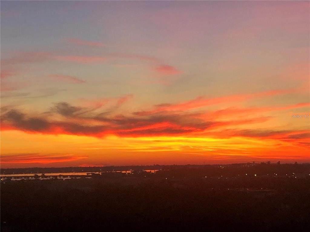 A vibrant sunset glows over a dark, silhouetted landscape with a distant body of water — 501 HABEN BOULEVARD UNIT 704, PALMETTO, FL