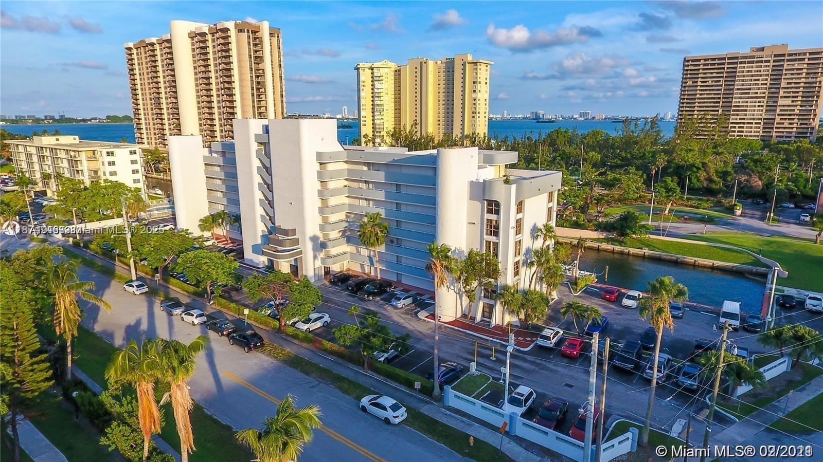An aerial view shows a white multi-story apartment building with a parking lot and canal — 1650 NE 115th St # 403, Miami FL 33181, MIAMI, FL