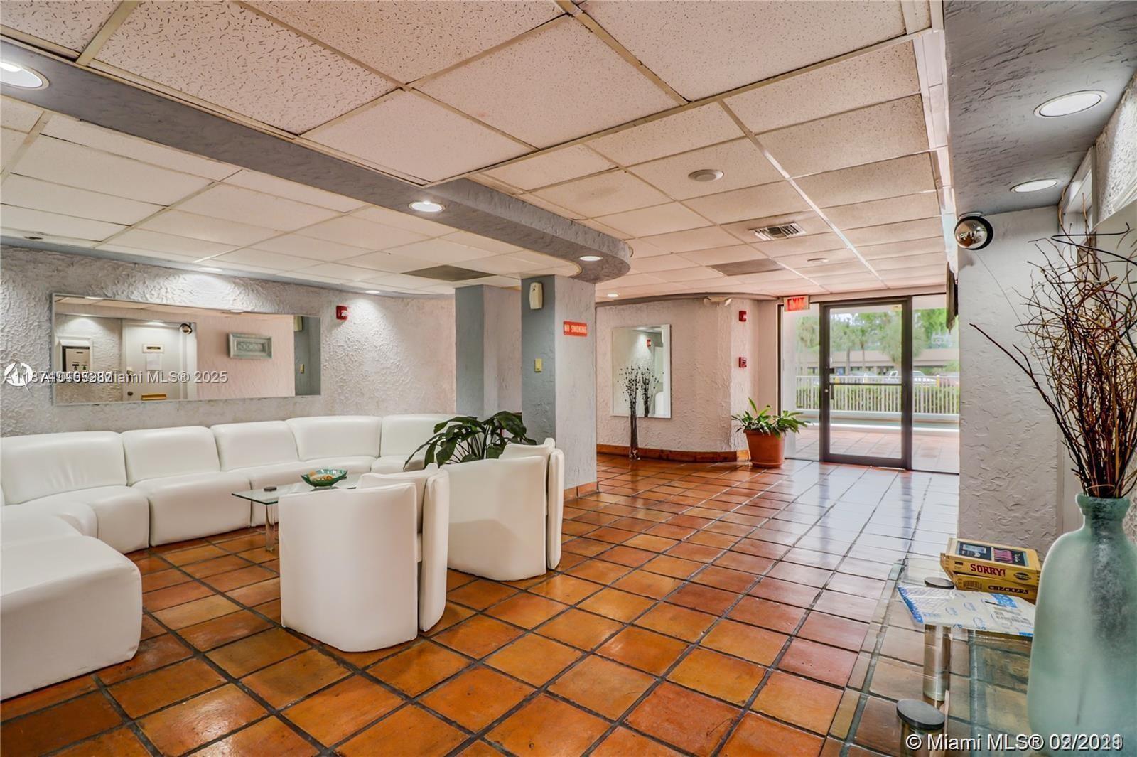 A lobby area features a white sectional sofa, tiled floors, and a glass exit door — 1650 NE 115th St # 403, Miami FL 33181, MIAMI, FL