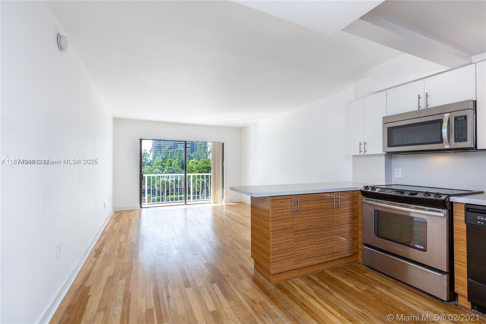 An open-concept kitchen with wood-grain cabinets and stainless steel appliances overlooks a living area — 1650 NE 115th St # 403, Miami FL 33181, MIAMI, FL